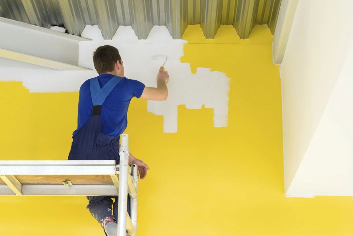 A painter rolling a fresh white coat over a yellow wall